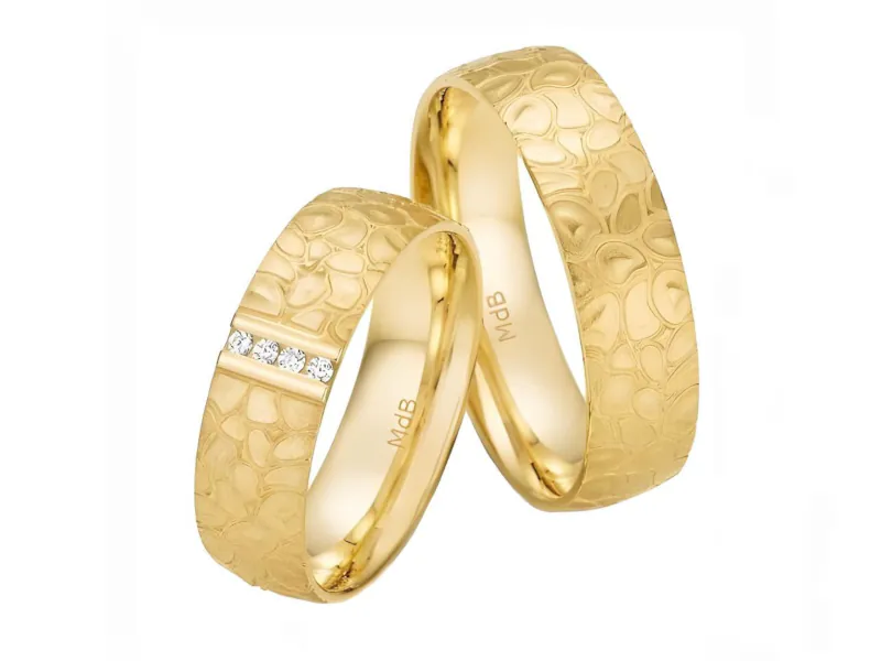 Par de anillos de matrimonio en oro amarillo con grabado, uno de ellos adornado con piedras.