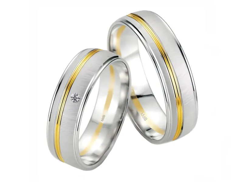 Par de anillos de boda en oro blanco con línea central de oro amarillo; el anillo más pequeño tiene una piedra incrustada