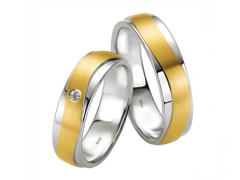 Par de anillos de boda con base de oro blanco y franja central de oro amarillo mate. El anillo más delgado incluye un piedra engastada en la sección dorada.
