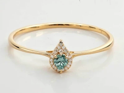 Anillo de promesa en oro 18k con piedra verde central en forma pera y halo de piedras, diseño delicado y elegante.