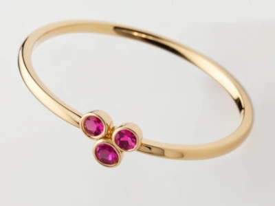 Anillo de promesa en oro amarillo 18k con tres piedras color granate engastadas en bisel, diseño delicado y moderno.