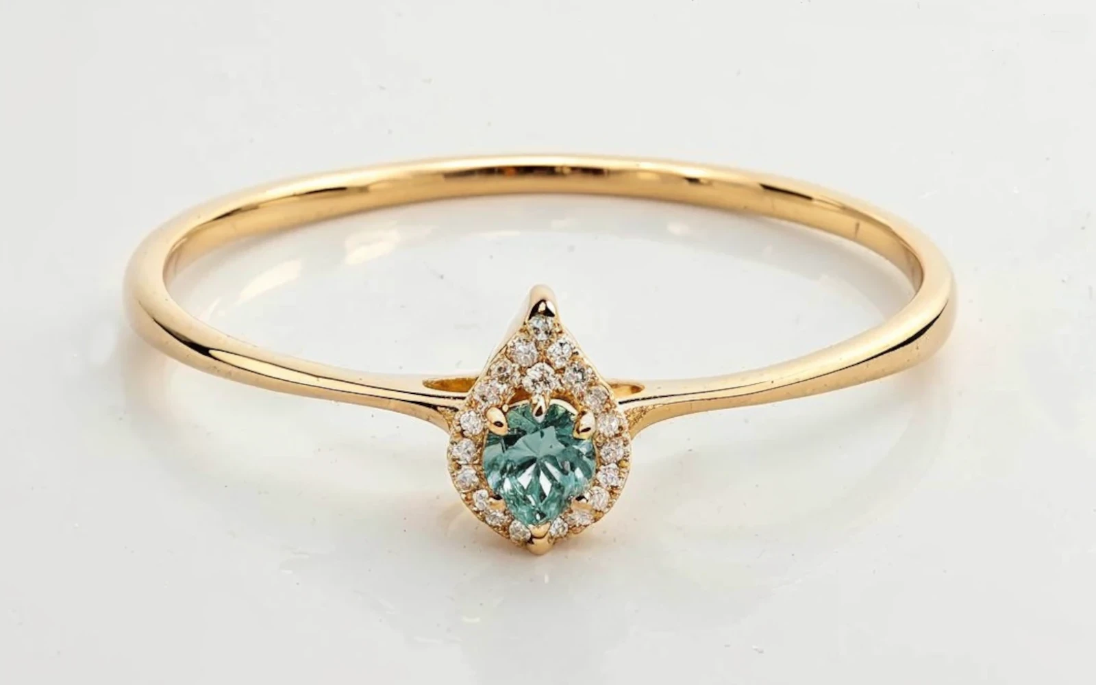 Anillo de promesa en oro 18k con piedra verde central en forma pera y halo de piedras, diseño delicado y elegante.