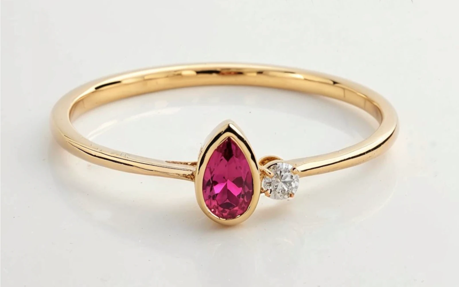 Anillo de promesa en oro amarillo 18k con piedra granate en forma pera y piedras laterales en diseño minimalista.
