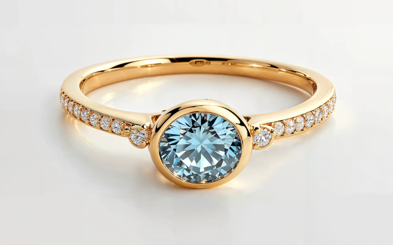 Anillo de promesa en oro amarillo 18k con piedra azul central redonda y piedras laterales en pavé fino.