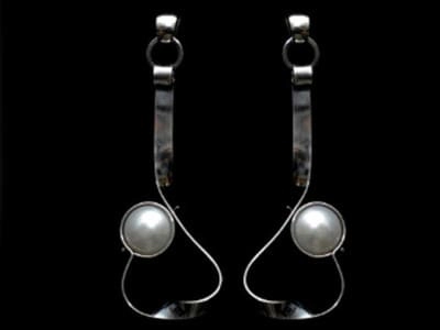 Pendientes de plata con perlas naturales. Esta imagen ilustra la belleza y delicadeza de las perlas, reforzando la importancia del cuidado adecuado que se describe en el post Cuidado para las Perlas Naturale. El fondo negro realza el brillo perlado y la elegancia del diseño.