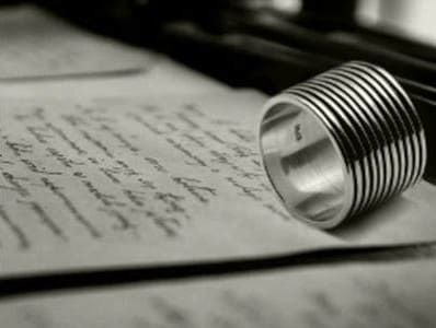 Imagen en blanco y negro de un anillo moderno con diseño acanalado sobre una carta manuscrita, simbolizando la fusión entre la joyería contemporánea y las emociones personales