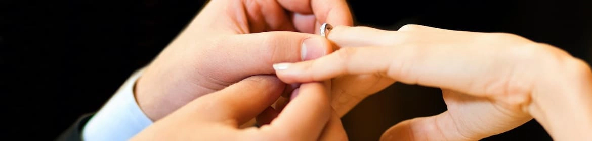 Manos de una pareja intercambiando anillos de boda en una ceremonia, simbolizando el compromiso y la unión.