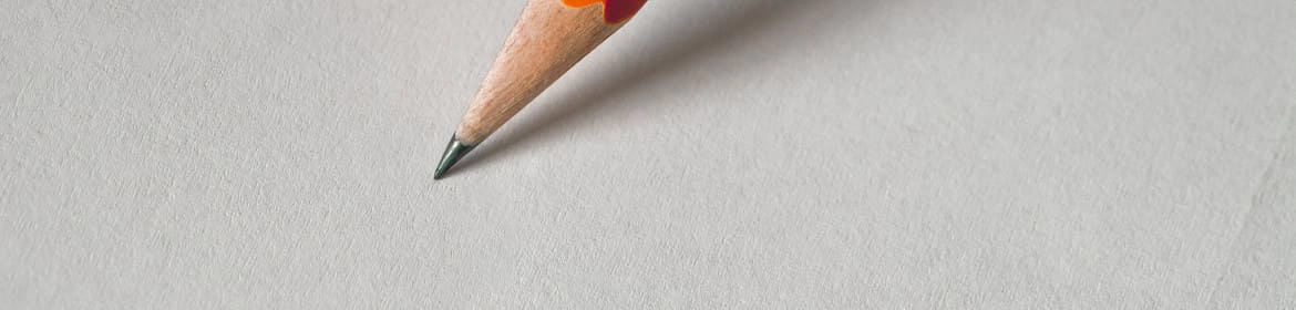 Primer plano de un lápiz de grafito con detalles en rojo y naranja, apoyado sobre una superficie gris clara, simbolizando el inicio del proceso de diseño