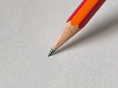 Primer plano de un lápiz de grafito con detalles en rojo y naranja, apoyado sobre una superficie gris clara, simbolizando el inicio del proceso de diseño