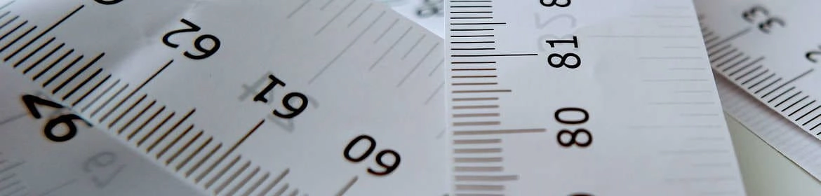 Imagen de primer plano de varias cintas métricas y reglas, herramientas esenciales para la toma de medidas precisas en joyería. Esta imagen ilustra la importancia de la exactitud en el diseño, la creación y el ajuste de joyas, tema central del post Medidas Útiles en Joyería.
