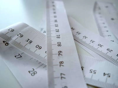 Imagen de primer plano de varias cintas métricas y reglas, herramientas esenciales para la toma de medidas precisas en joyería. Esta imagen ilustra la importancia de la exactitud en el diseño, la creación y el ajuste de joyas, tema central del post Medidas Útiles en Joyería.