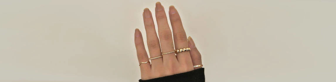 Mano mostrando varios anillos de oro en diferentes estilos, incluyendo diseños minimalistas y detalles decorativos, sobre un fondo neutro.