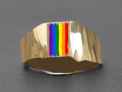 Un anillo de oro con una representación de la bandera del Orgullo LGBTQ+ en su superficie. El anillo tiene una banda ancha y plana, y la bandera está colocada verticalmente en el centro. El fondo es gris oscuro, lo que hace que el anillo dorado y los colores del arco iris destaquen.
