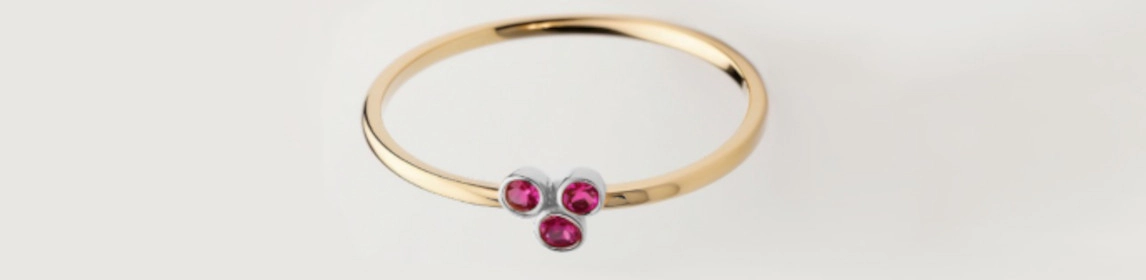 Anillo de oro amarillo con tres piedras preciosas de color rubí, exhibiendo un diseño elegante y contemporáneo.