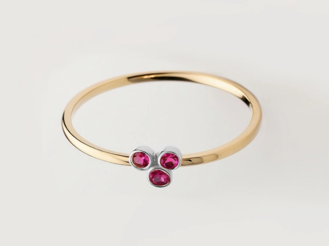 Anillo de oro con piedras preciosas Anillo de oro amarillo con tres piedras preciosas de color rubí, exhibiendo un diseño elegante y contemporáneo.