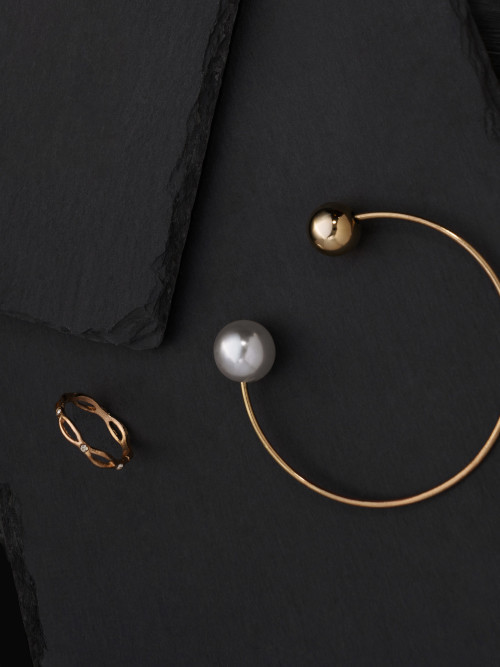 Elegante brazalete dorado con perlas y un delicado anillo de oro sobre un fondo negro. Representa la sofisticación y la calidad de las joyas Malena de Botana.